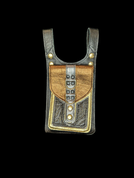 A thigh bag with one large pocket. Base is made with a black leather. Pocket base is made with a gold leather with silver and black & gold mosaic patterned leather accents. The pocket flap is made with a bronze leather with a silver strip. Includes black stitching and black & gold hardware.