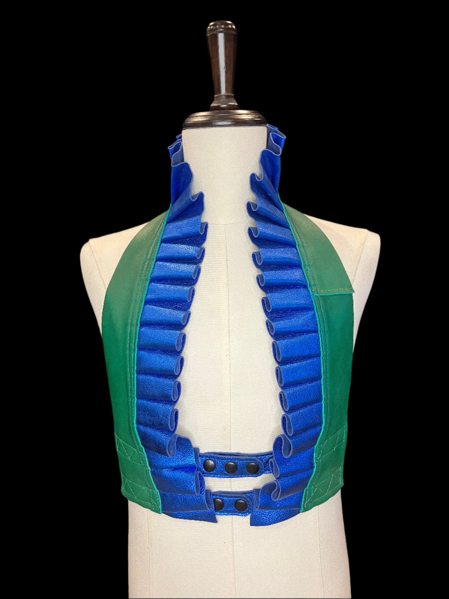 Ruff top with green leather neck and metallic blue leather ruff and black hardware on an ivory gender neutral mannequin against a black background