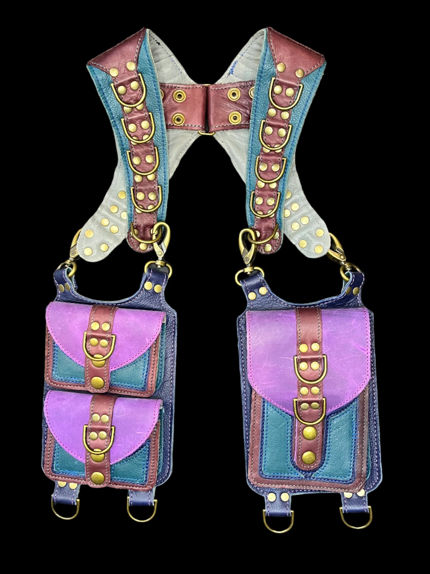 Wallflower holster in teal, maroon, and purple with antique brass hardware laid flat on a black background