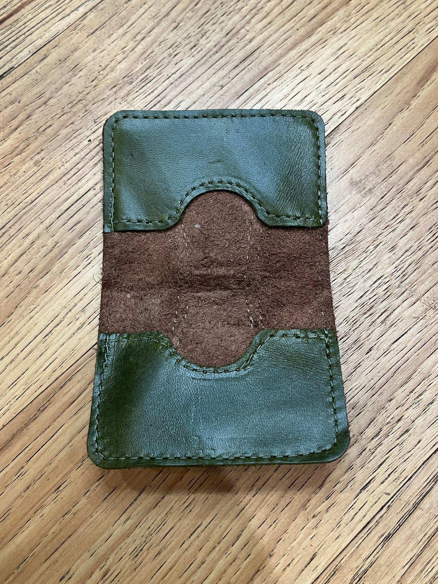 A wallet spread open showing a base color of brown leather with two card pockets in dark green leather with green stitching.