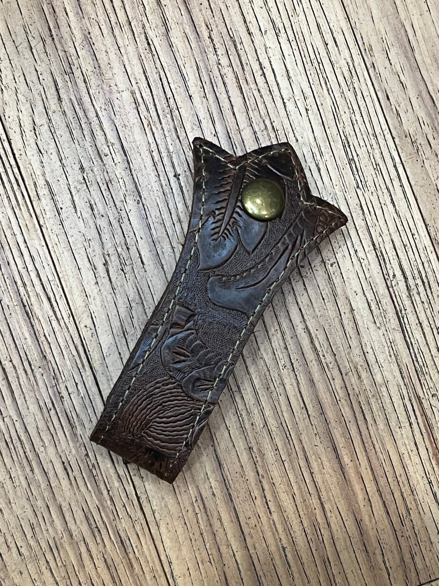 A trident shaped double layered mug frog using brown floral tooled leather, tan stitching and a brass snap.