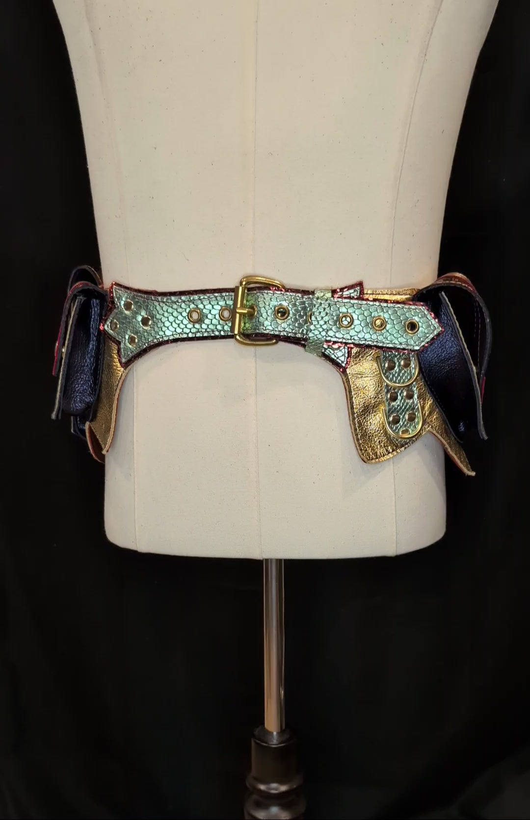 A 360 video of a regal belt on a mannequin with one large pocket and 3 smaller pockets made with a gold snake patterned leather with  dark green accent and flaps made with a red snake patterned leather with a gold leather accent. Pockets have a blue gusset and gold hardware.