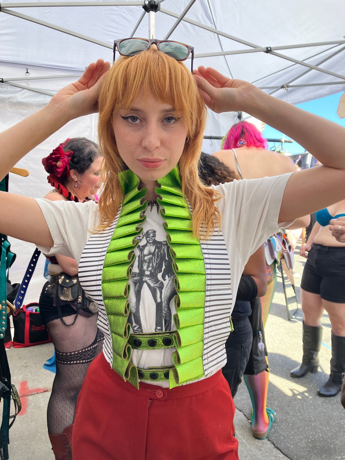 femme caucasian individual with short red hair wearing a graphic t-shirt and red pants sporting a Showtime Ruff, looking at the camera while in the processes of raising her sunglasses.