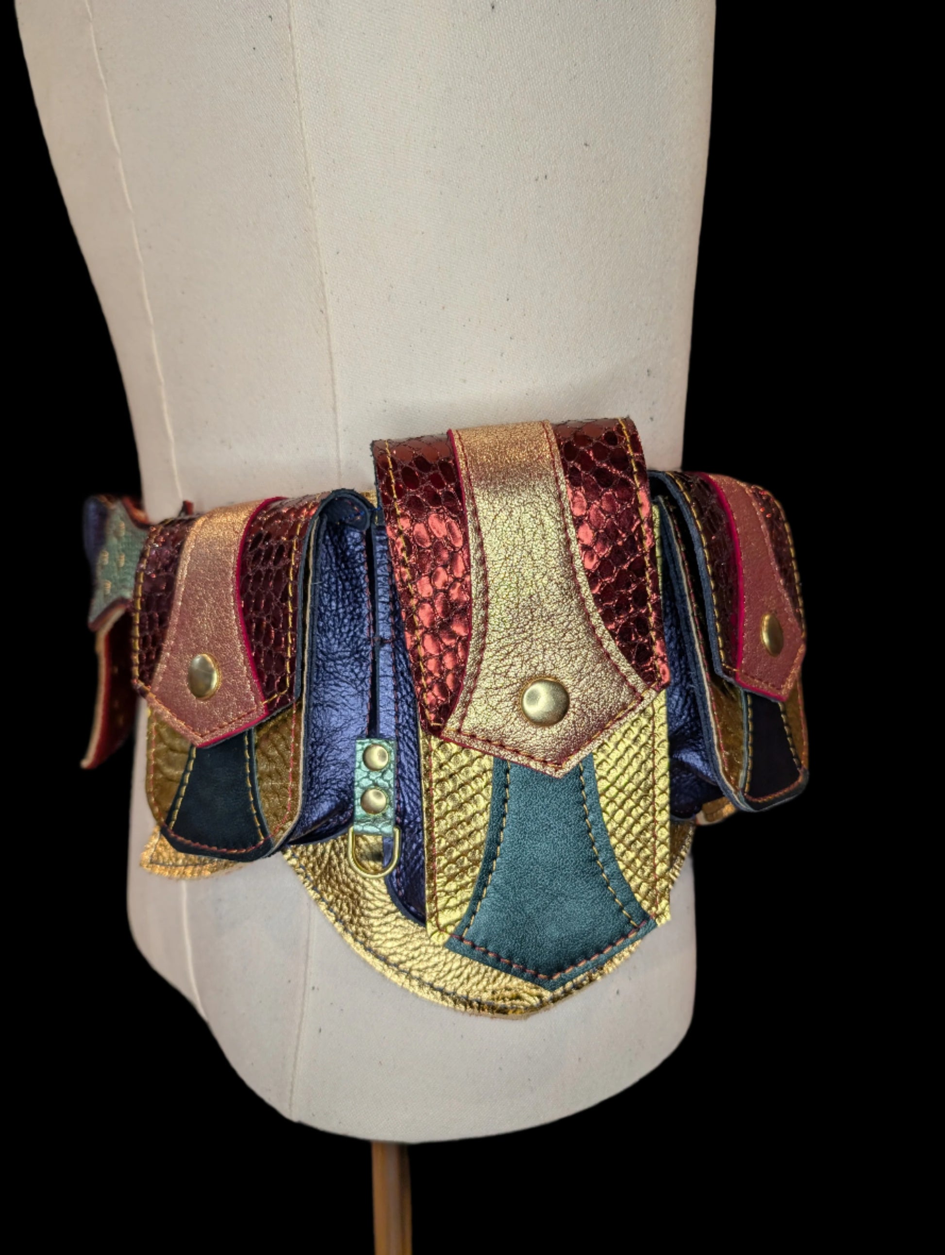 A regal belt on a mannequin with one large pocket and 3 smaller pockets made with a gold snake patterned leather with  dark green accent and flaps made with a red snake patterned leather with a gold leather accent. Pockets have a blue gusset and gold hardware.