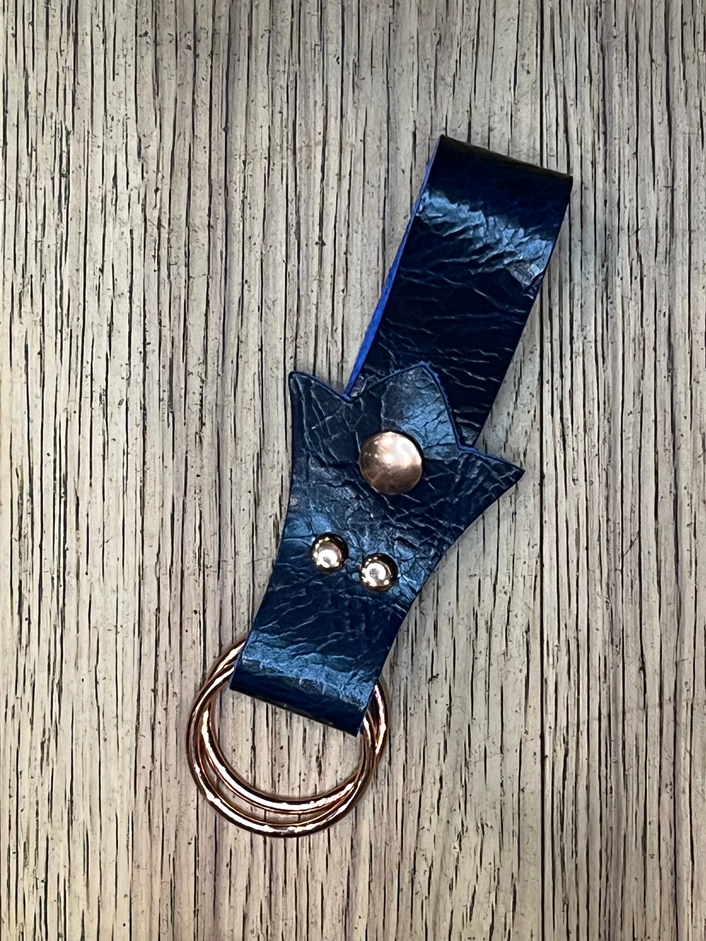 A skirt hike made with dark blue leather in a trident shape with rose gold snaps and rings. 