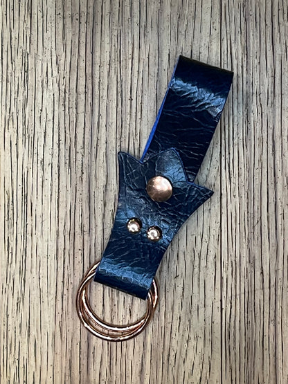 A skirt hike made with dark blue leather in a trident shape with rose gold snaps and rings. 
