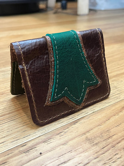 A wallet folded in half showing a base color of brown leather with a layered trident accent in dark green and brown floral leather with green and brown stitching. 
