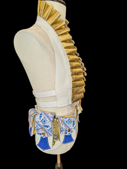 A photo of a white and gold ruffle top and a regal belt that has one large pocket and 3 small pockets made with a white and blue floral leather with gold cracks through out the flaps. A white base and dark blue accents, gold gusset and gold hardware. 