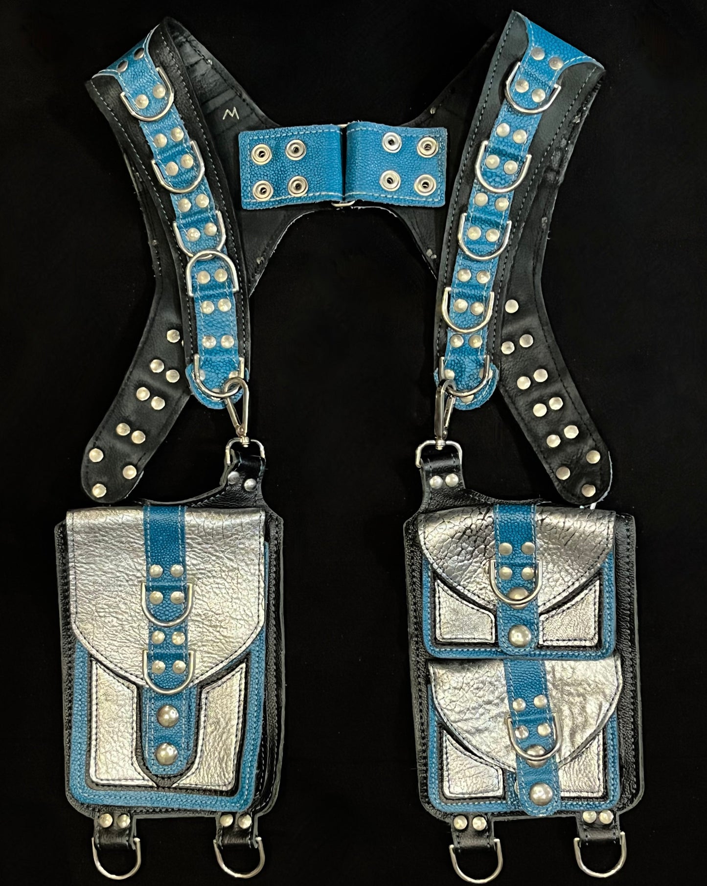 front view of black, teal, and silver leather holster with hanging pockets and nickel hardware