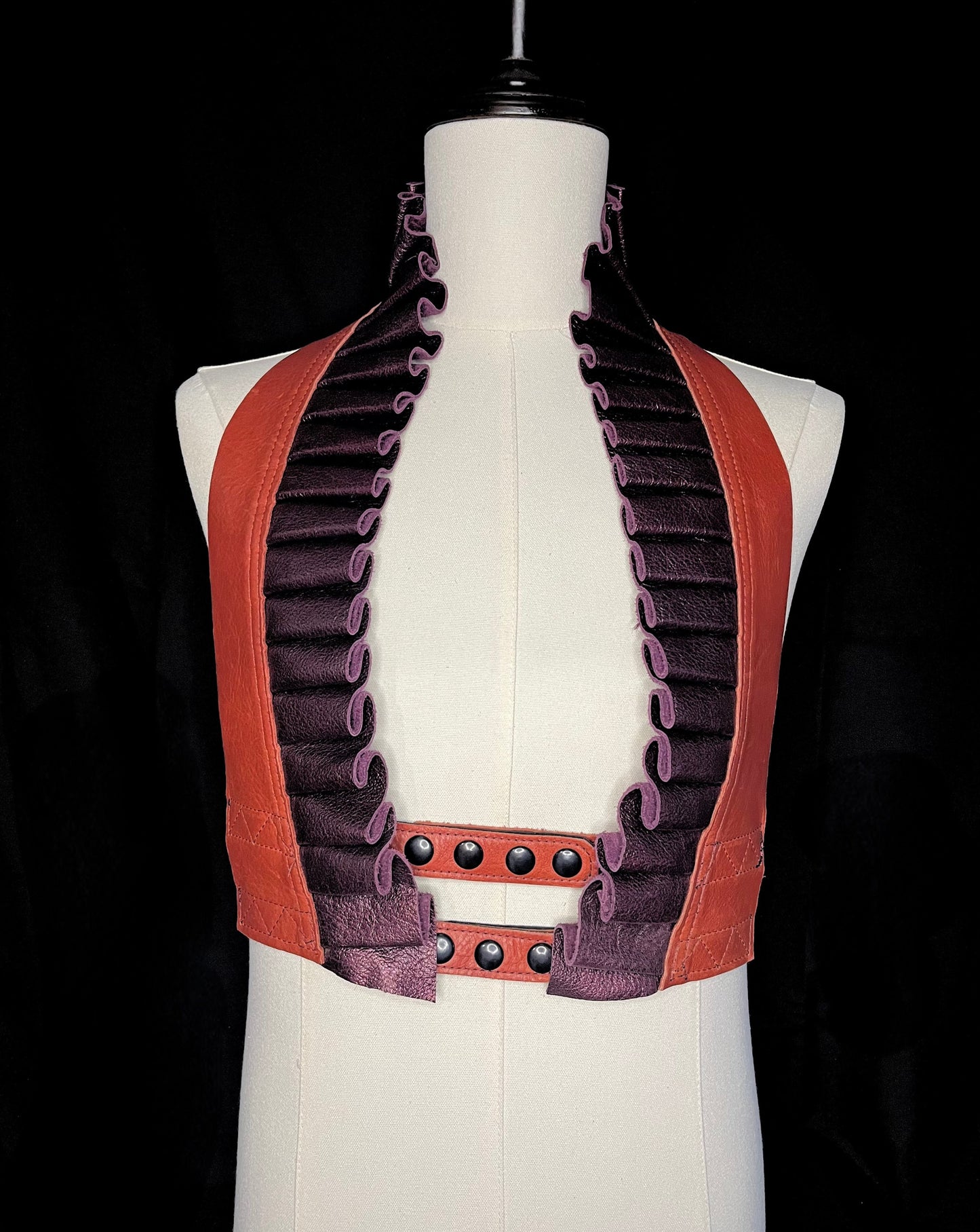 vermillion orange and metallic maroon leather ruff top with black hardware on an ivory gender neutral mannequin against a black background