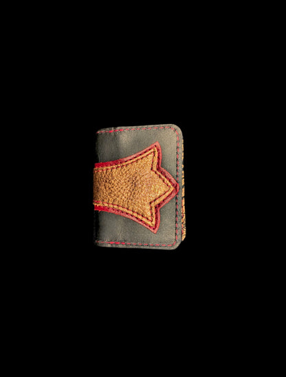 A wallet folded in half showing a base color of black  leather with a layered trident accent in red and bronze leather with red stitching. 