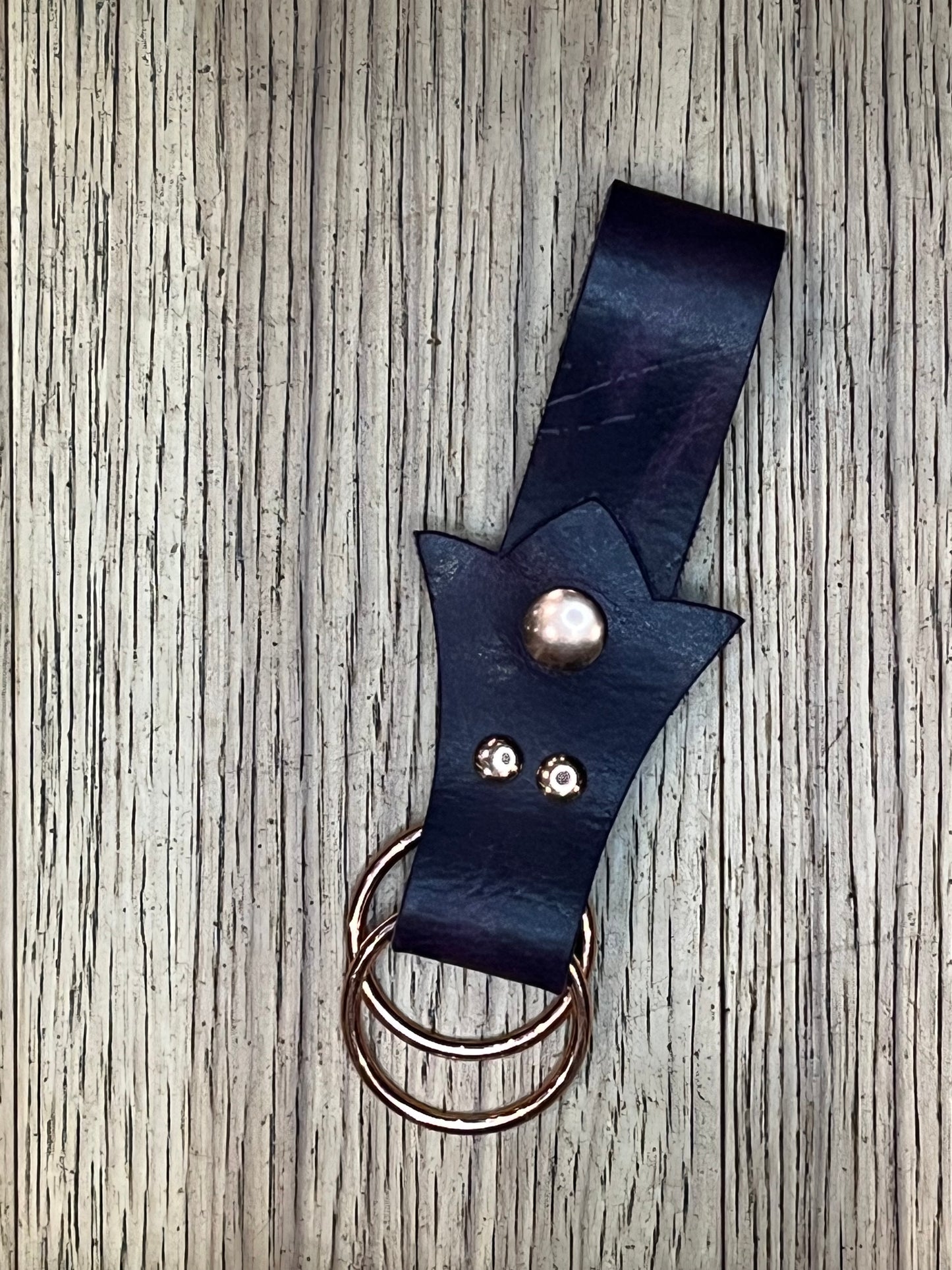 A skirt hike made with dark purple leather in a trident shape with rose gold snaps and rings. 