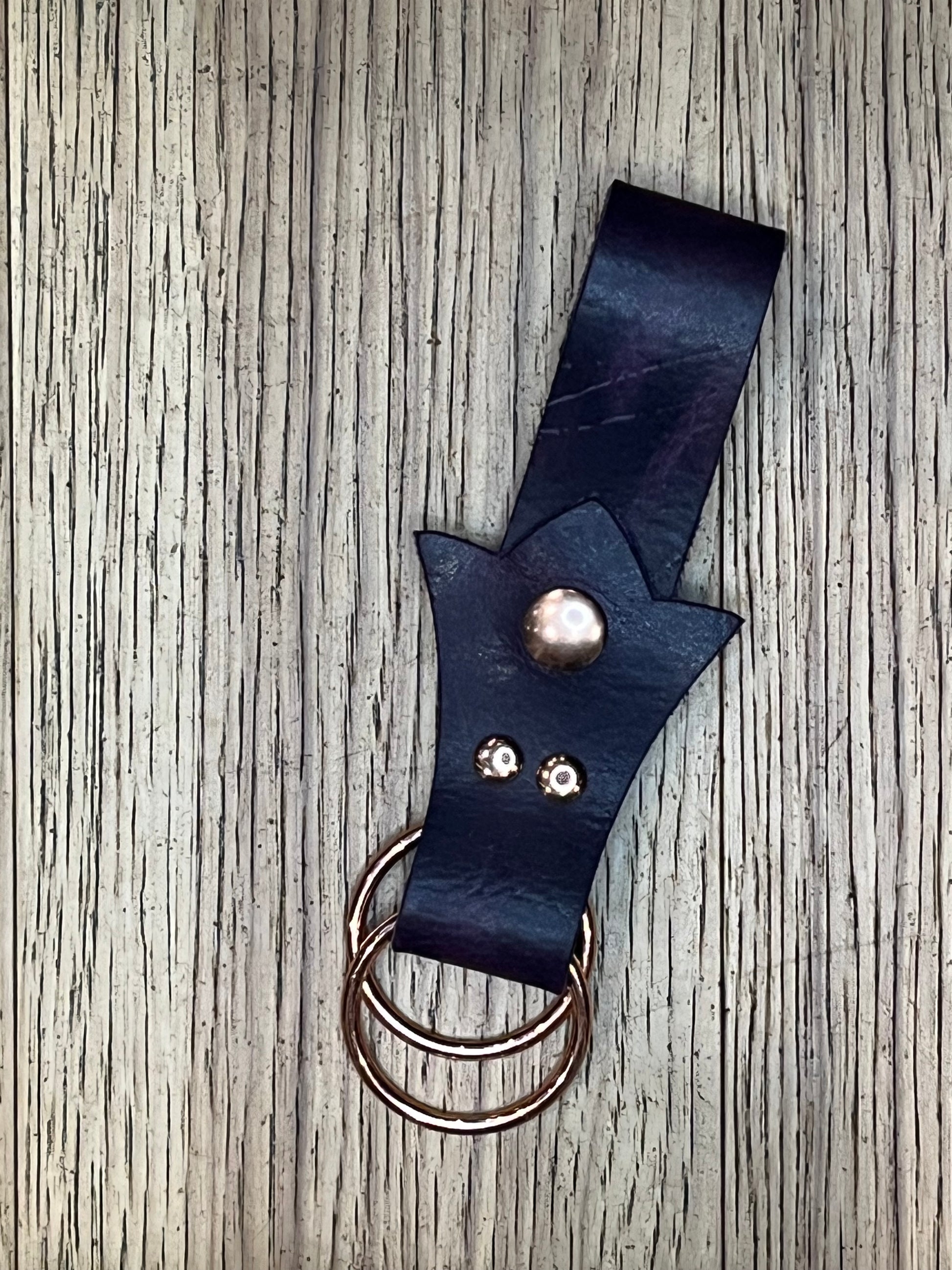 A skirt hike made with dark purple leather in a trident shape with rose gold snaps and rings. 