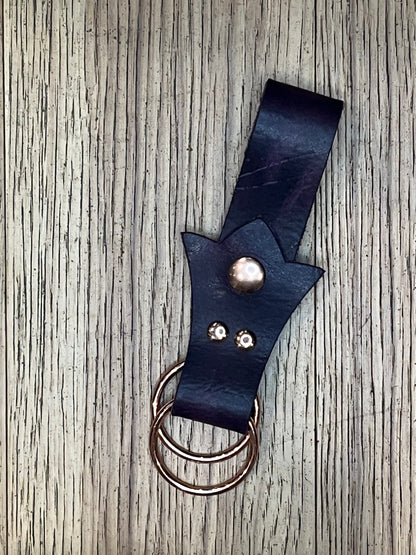 A skirt hike made with dark purple leather in a trident shape with rose gold snaps and rings. 