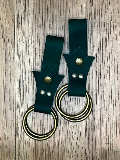 A pair of skirt hikes made with dark green leather in a trident shape with brass snaps and rings. 
