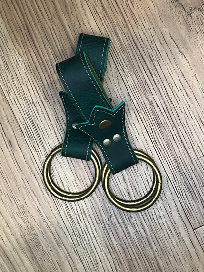 A pair of shmancy skirt hikes made in a trident shape with  a double layer of dark green leather, light green stitching and brass snaps and rings. 
