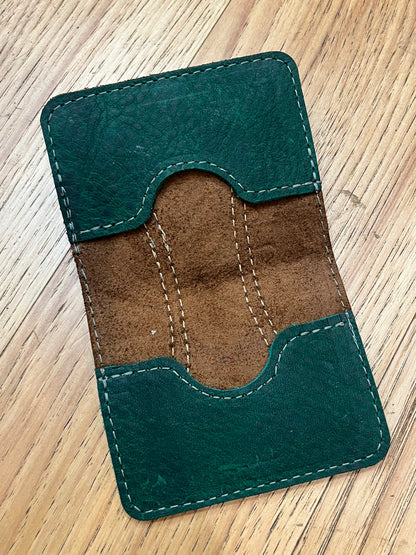 A wallet spread open showing a base color of brown leather with two card pockets in dark green leather with green stitching. 