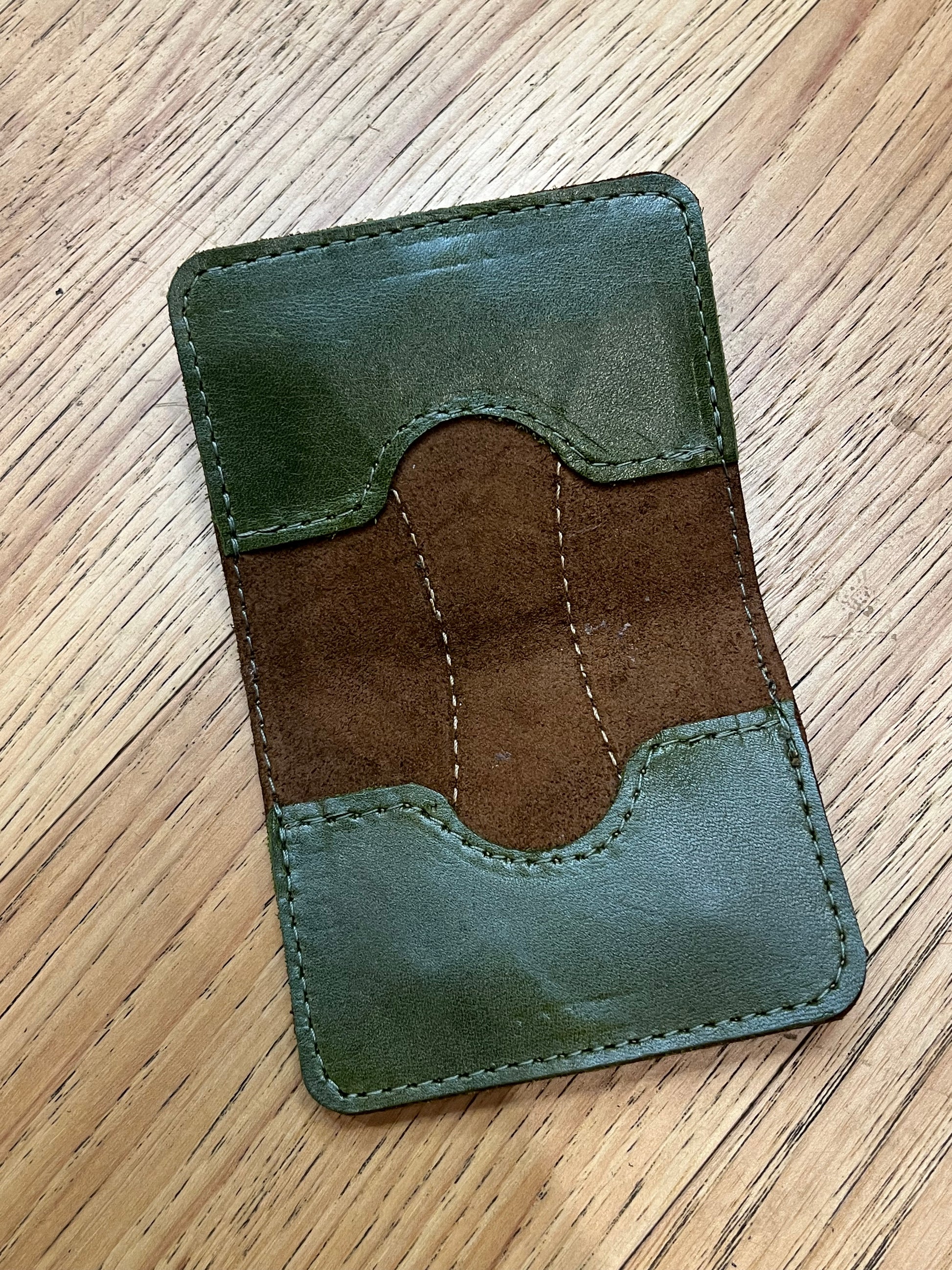 A wallet spread open showing a base color of brown leather with two card pockets in dark green leather with green stitching. 