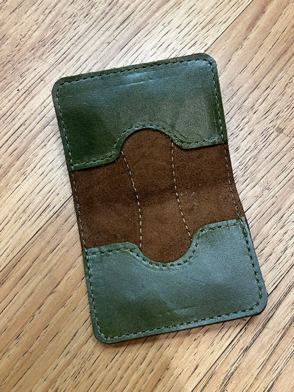 A wallet spread open showing a base color of brown leather with two card pockets in dark green leather with green stitching. 