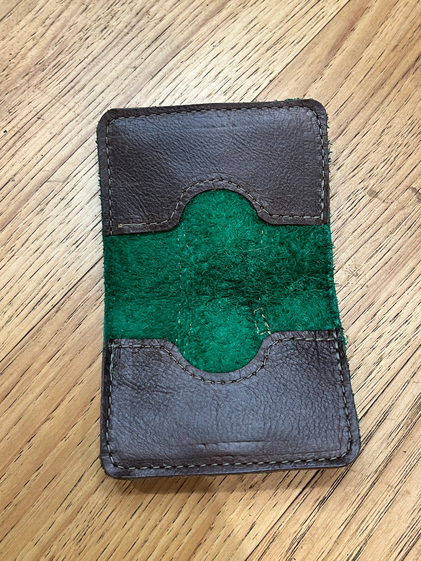 A wallet spread open showing a base color of dark green leather with two card pockets in brown leather with green stitching.