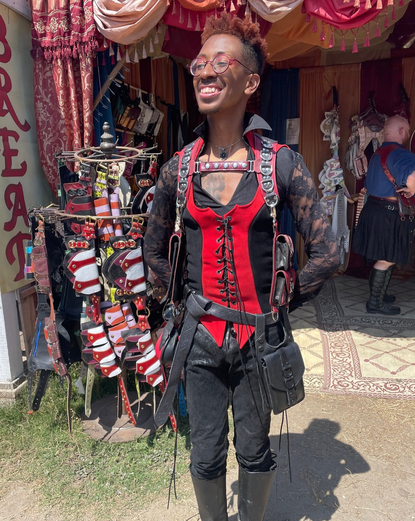 individual standing in front of the booth showing a red and black leather holster with a custom chest strap, smiling looking off camera. 