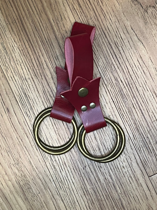 A pair of skirt hikes made with red leather in a trident shape with brass snaps and rings. 
