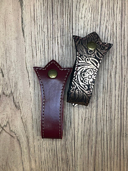 Two mug frogs in a trident shape. One is bronze floral leather with red stitching and the other is dark ed leather with bronze stitching. 