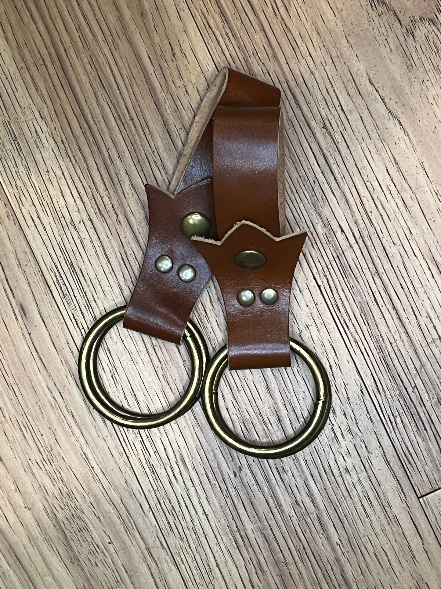 A pair of skirt hikes made with brown leather in a trident shape with brass snaps and rings. 
