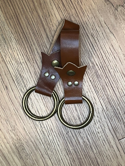 A pair of skirt hikes made with brown leather in a trident shape with brass snaps and rings. 
